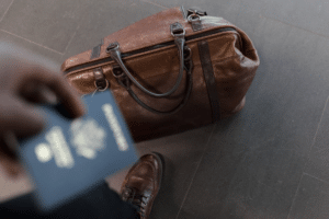 Person holds passport with travel bag and shoe nearby.