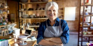Senior woman wearing an apron and standing with arms crossed in her store