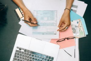 Person filling out a 1040 tax form with a pen next to a laptop.