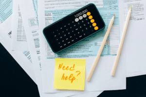Tax form, calculator showing 1,000,000, pencils, and sticky note reading 'Need help?'