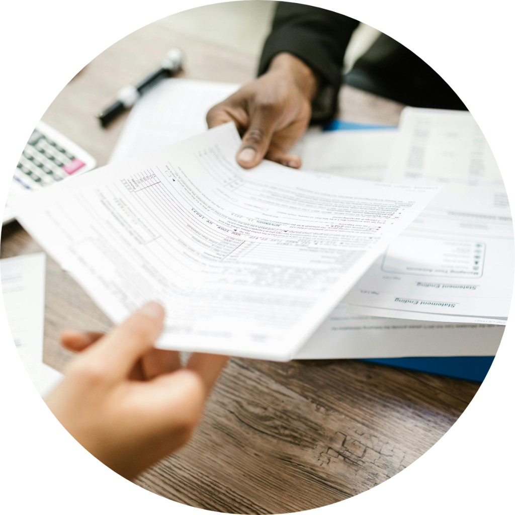 Tax advisor handing financial documents to client across desk during tax preparation consultation, with calculator and bank statements in background