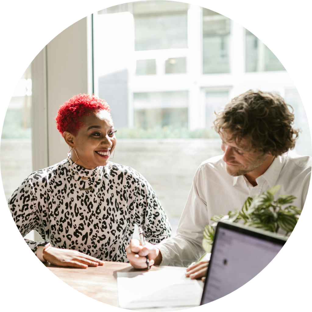 Smiling female financial advisor consulting with male client at office desk with laptop during tax planning or financial strategy meeting