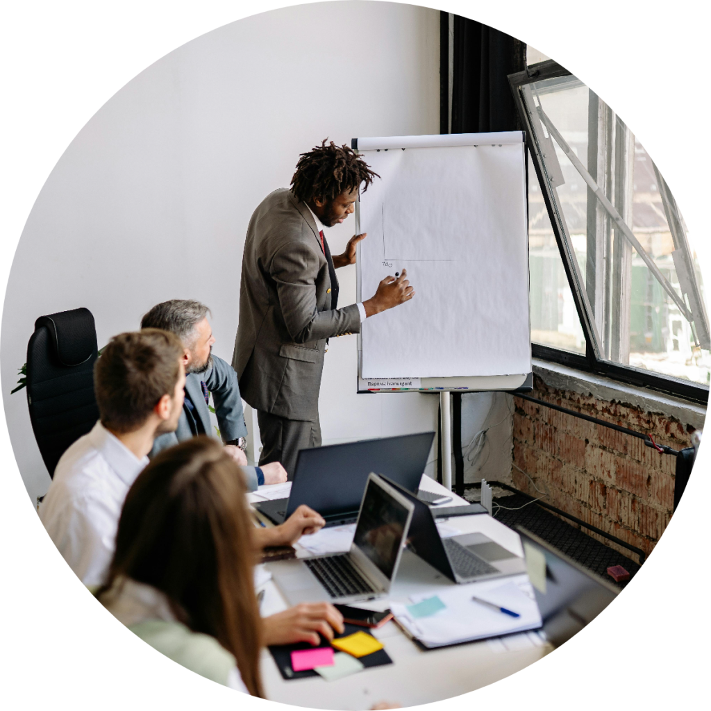 Business professional presenting financial strategy on whiteboard flipchart to team of colleagues with laptops during corporate training or tax planning workshop