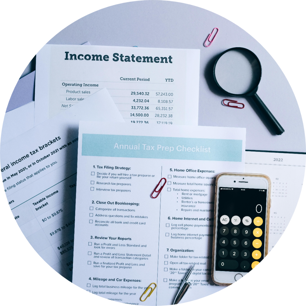 Annual tax prep checklist and income statement documents with calculator app, magnifying glass, and federal income tax bracket chart for small business tax filing preparation