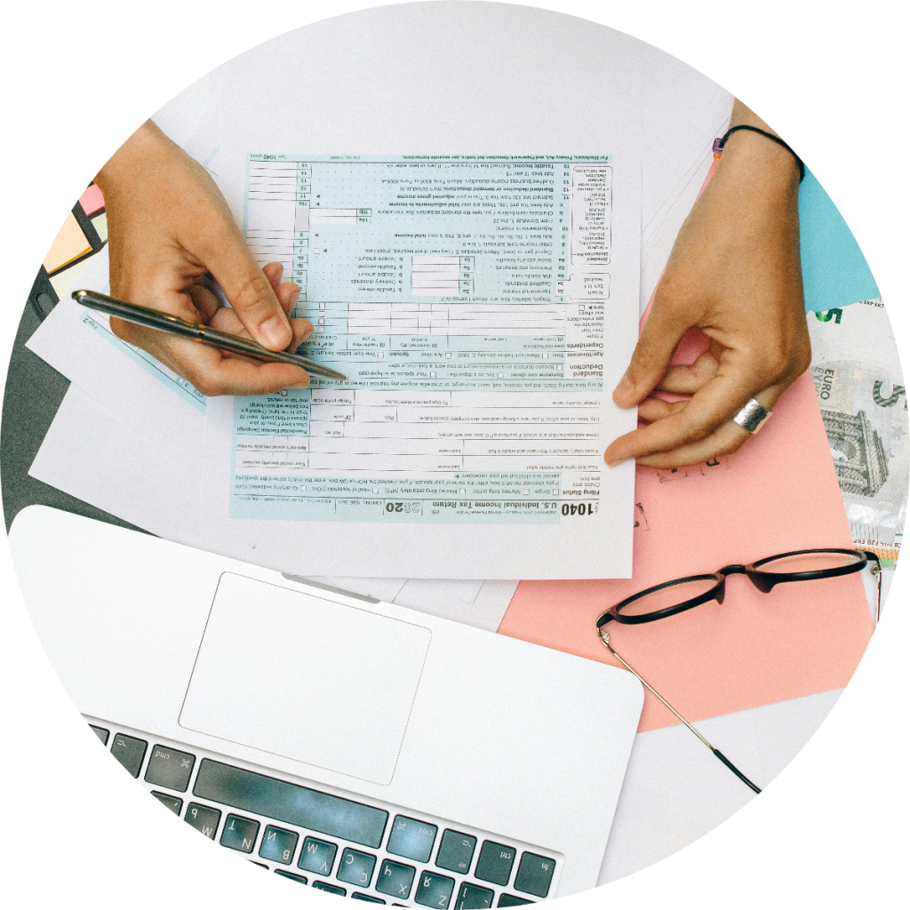 Tax professional reviewing IRS Form 1040 U.S. Individual Income Tax Return with laptop, glasses, and euro currency notes during annual federal tax filing preparation