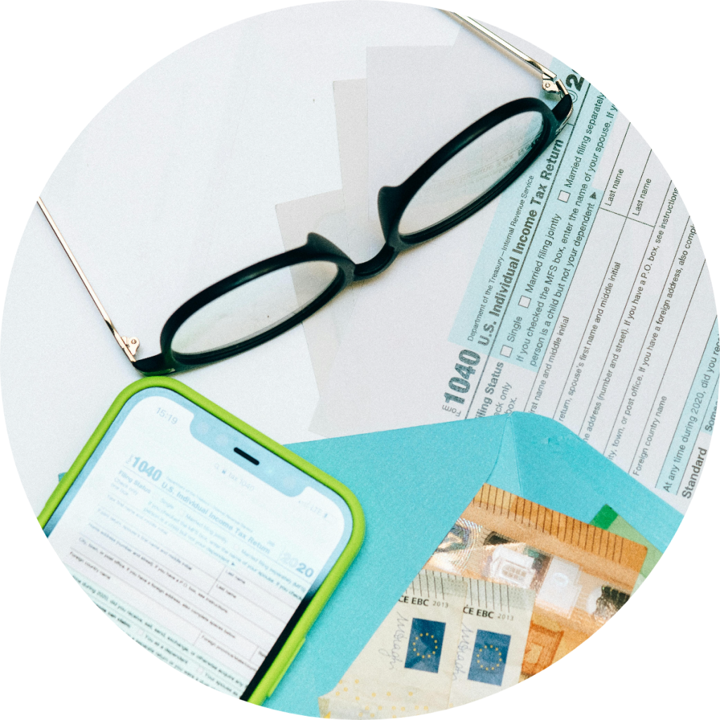 IRS Form 1040 U.S. Individual Income Tax Return displayed on smartphone and paper document alongside reading glasses and euro currency notes for digital tax filing preparation