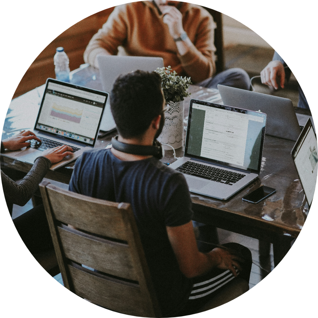 Diverse small business team working on multiple laptops with financial dashboards and spreadsheets at shared coworking space table during collaborative tax planning or bookkeeping session